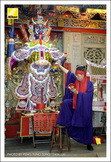 七月十八日晚上，法師以朱筆為大士爺、山神、土地等開光點眼；民間俗稱大士爺為「鬼王」，主要職司為安撫並壓制前來普渡會場的孤魂野鬼以免為亂。（Nikon D2X，ISO 400，AF-S 17-55mm F2.8G鏡頭，焦距32mm，f2.8光圈先決，快門1/40秒）