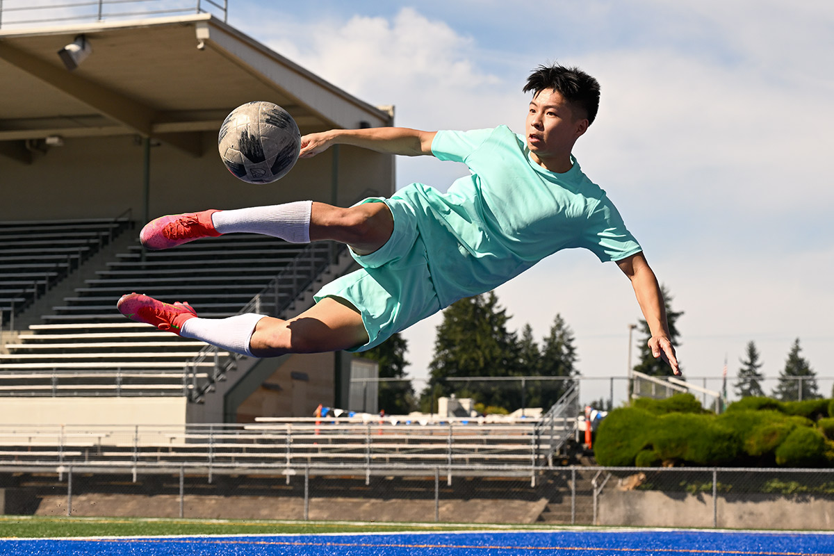 Photo of a soccer player in mid kick in air, horizontal to the ground